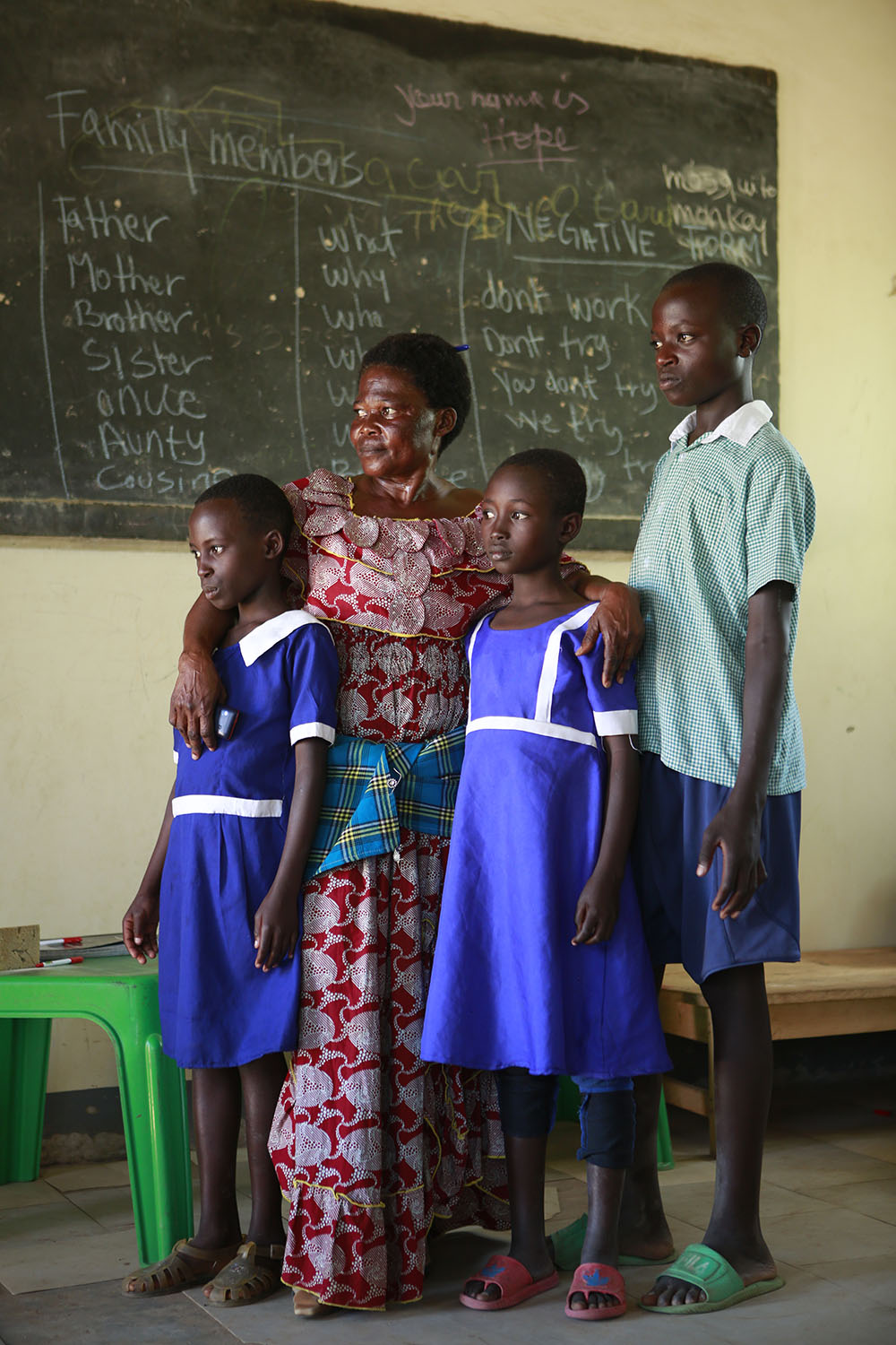 Francoise Mukundu, a teacher at the primary school in Kabazana Reception Centre, Nakivale Refugee Settlement, with three of her pupils, all wearing uniforms she has made for them on her days off.  “I want all my kids to be smart. When I make them uniforms and they get shoes, they are so happy. It makes the other kids want to come to school too.” Francoise is also a refugee, from Democratic Republic of Congo.  She lost her entire family in DRC and came alone to Uganda.